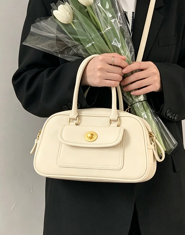 Close-up handheld view of off-white Minimalist Convertible Bag with gold turn-lock closure at Grandmama Store in Hong Kong