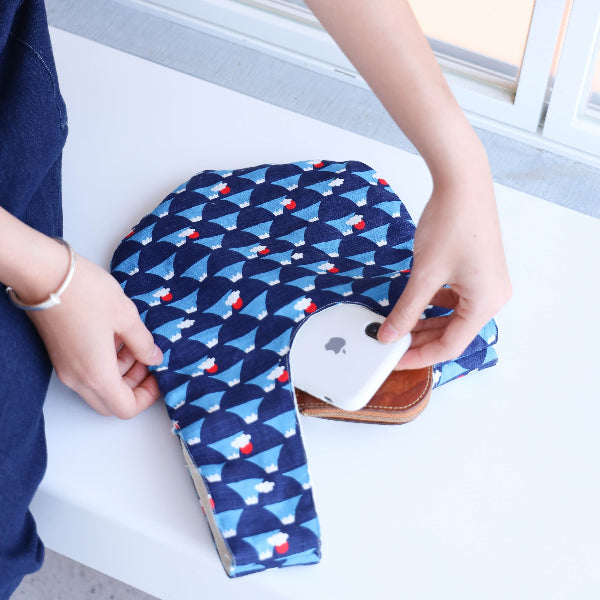 Hand placing a smartphone inside a blue Fuji Handled Moonshell Bag at Grandmama Store in Hong Kong.