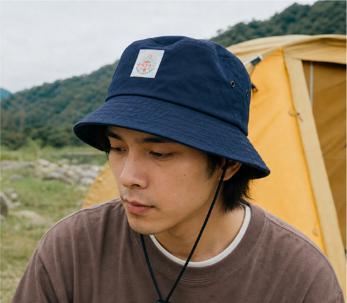 A close-up portrait of a male model wearing a dark navy blue Yama Workwear Bucket Hat from the Yama Series. The photo showcases the durable stitched brim texture, metal ventilation eyelets, front logo patch, and the black adjustable toggle chin strap attached under the chin as he looks thoughtfully to the side at Grandmama Store in Hong Kong.